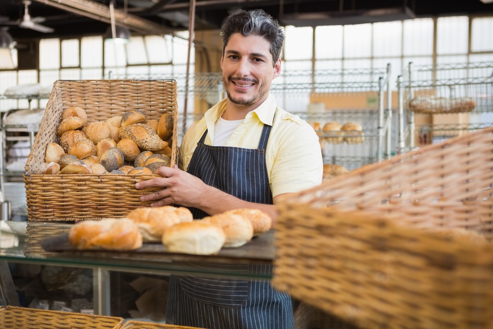 Portrait of happy worker holding basket of bread at the bakery